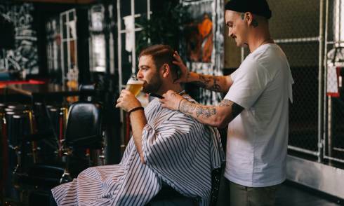 Person receiving a haircut and drinking a beer