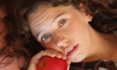 a closeup of a girl's face, her hair is spread around her as she holds an apple close to her face